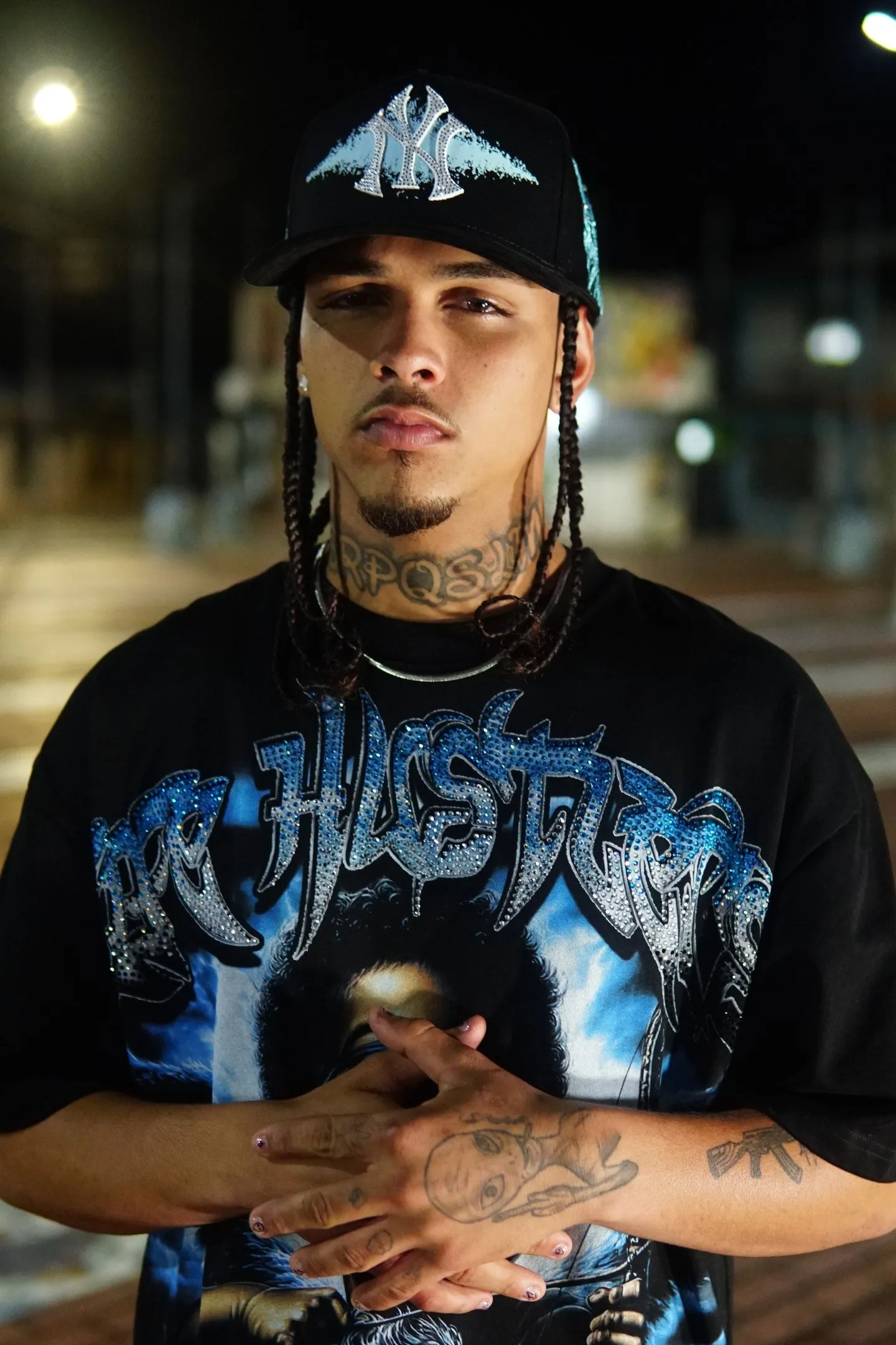 AM de noche en una calle de la ciudad, con una gorra de New York con strass y una camiseta de Hustlers